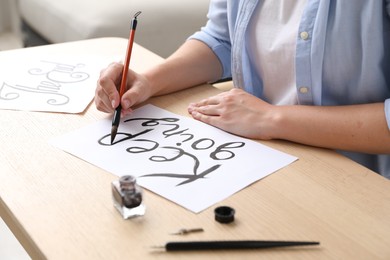Photo of Calligraphy. Woman with brush writing phrase Keep Going on sheet of paper at wooden table indoors, closeup