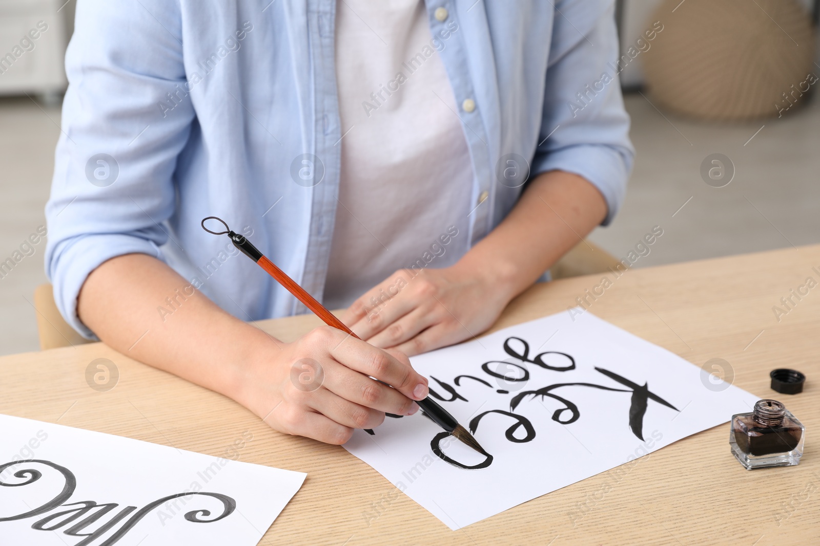 Photo of Calligraphy. Woman with brush writing phrase Keep Going on sheet of paper at wooden table indoors, closeup