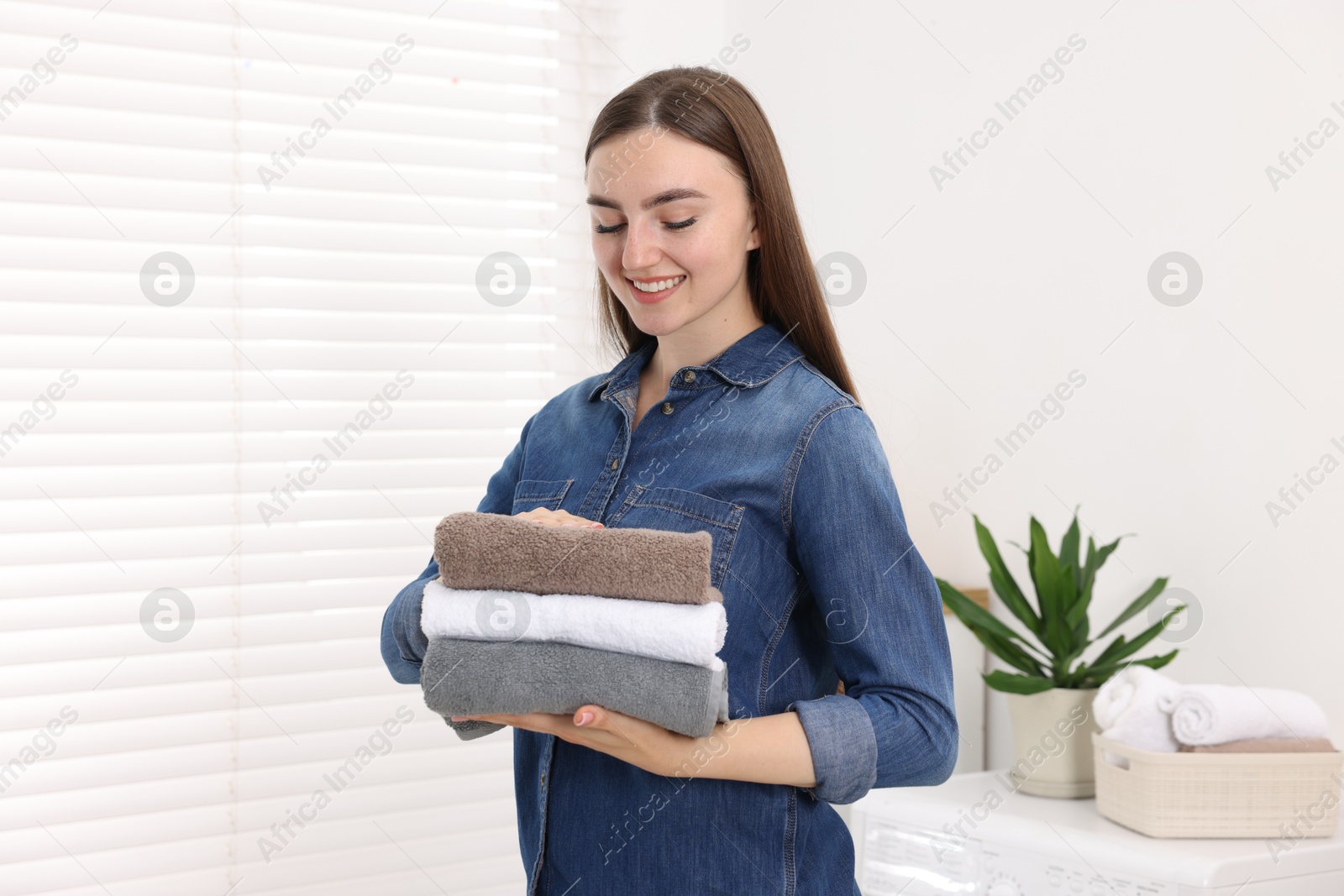 Woman with stack of clean laundry indoors Photo of Woman with stack of clean laundry indoors