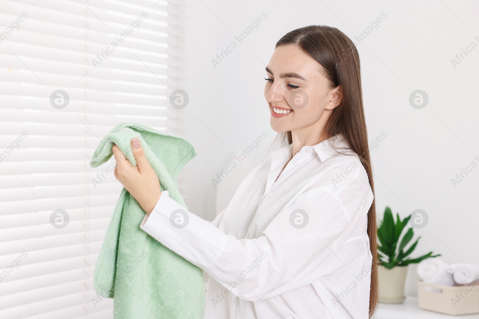 Woman with clean laundry near window indoors Photo of Woman with clean laundry near window indoors