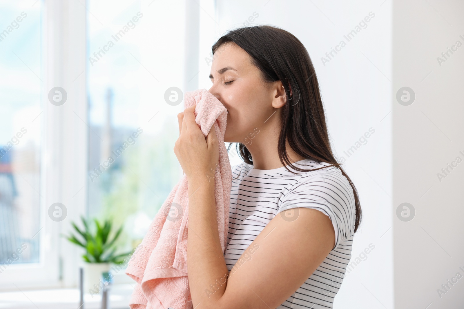 Photo of Woman with clean laundry near window indoors