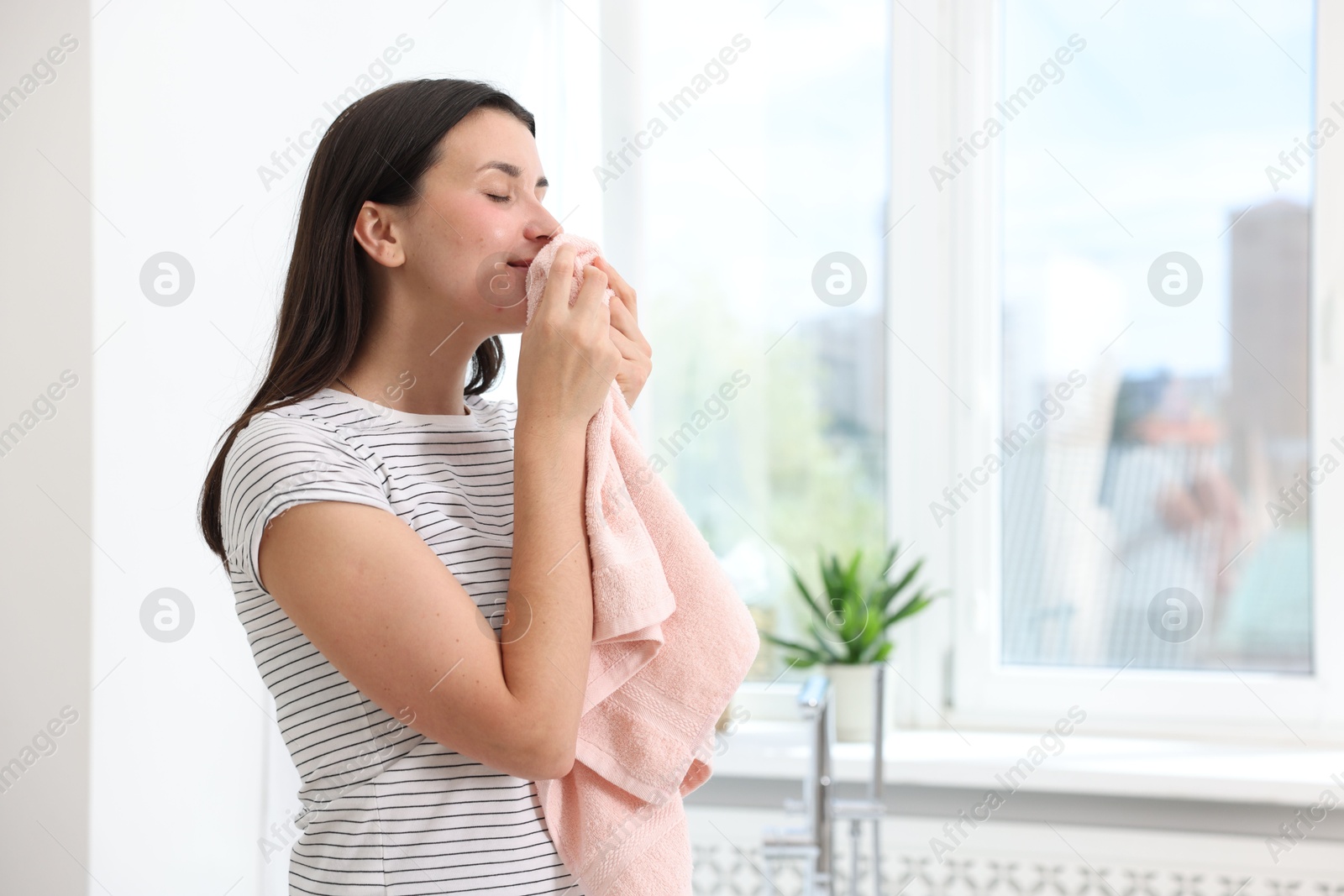 Woman with clean laundry near window indoors, space for text Photo of Woman with clean laundry near window indoors, space for text