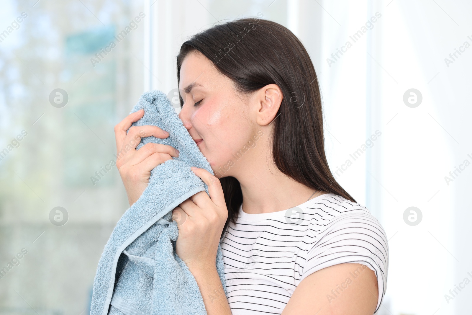 Photo of Woman with clean laundry near window indoors