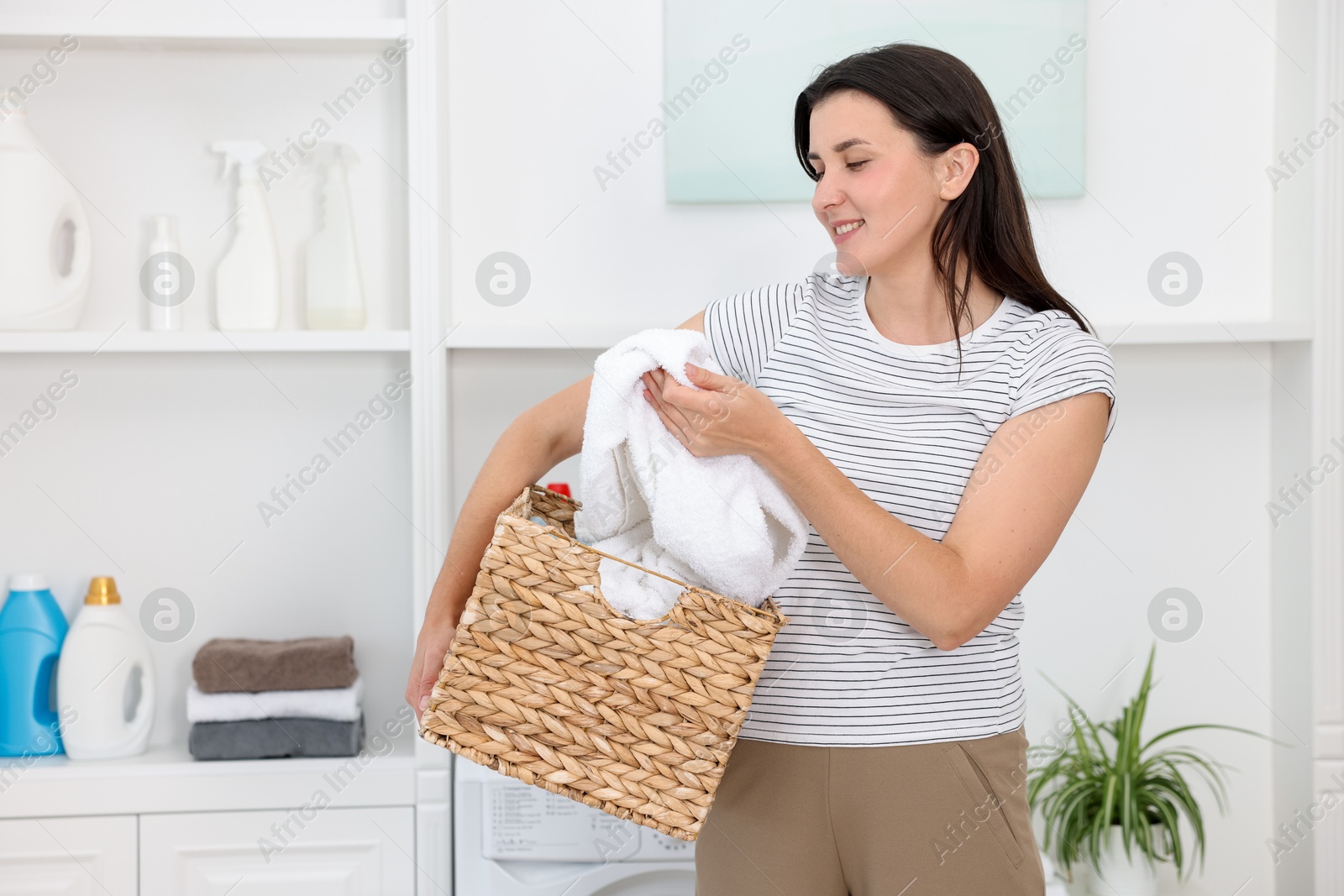 Photo of Woman with basket full of laundry indoors, space for text