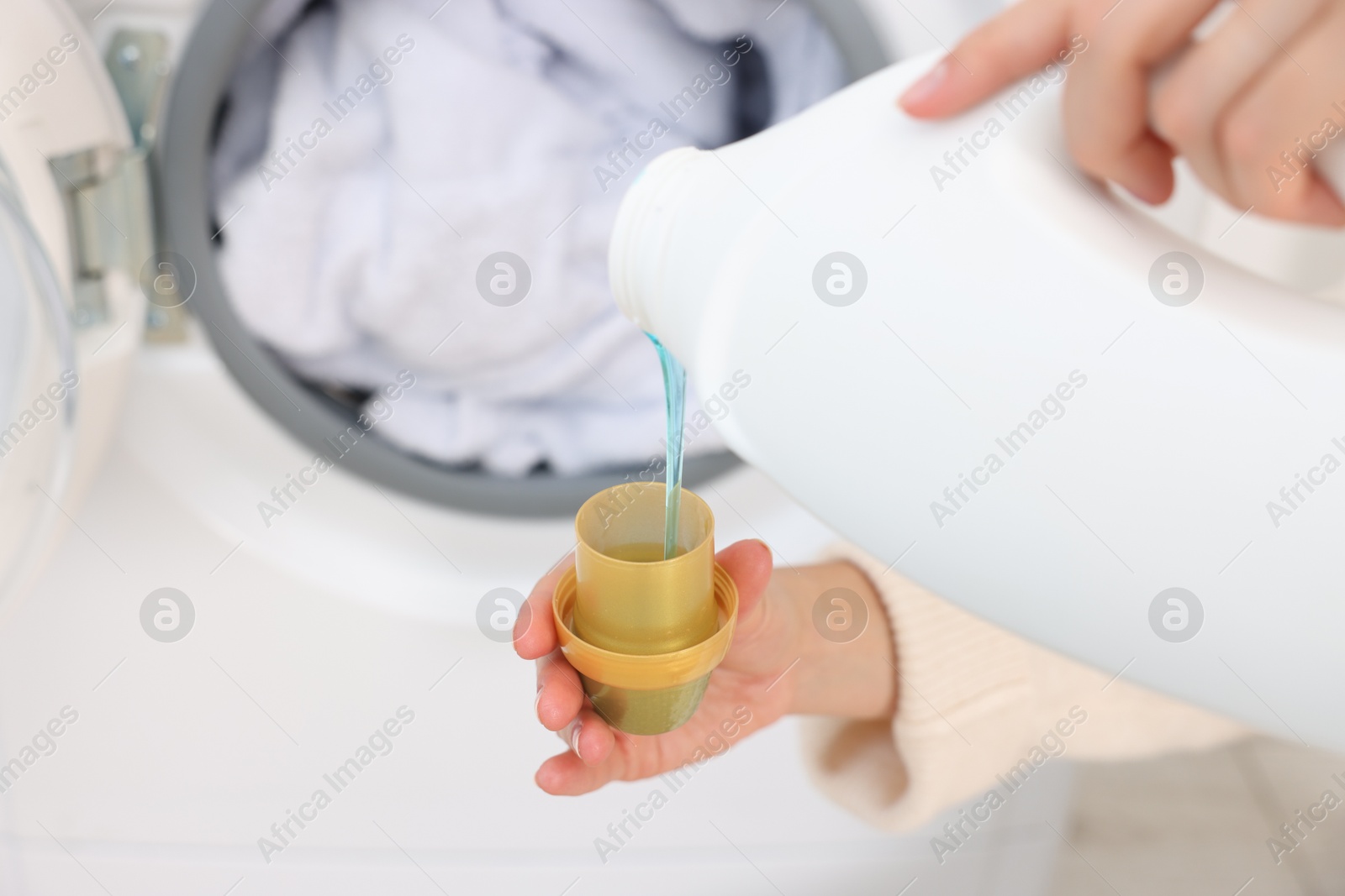 Photo of Woman pouring detergent into cap near washing machine indoors, closeup. Laundry day. Space for text
