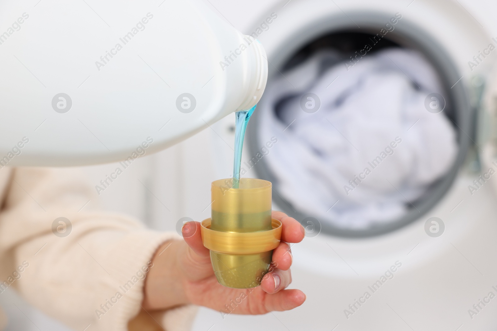 Photo of Woman pouring detergent into cap near washing machine in laundry room, closeup. Space for text