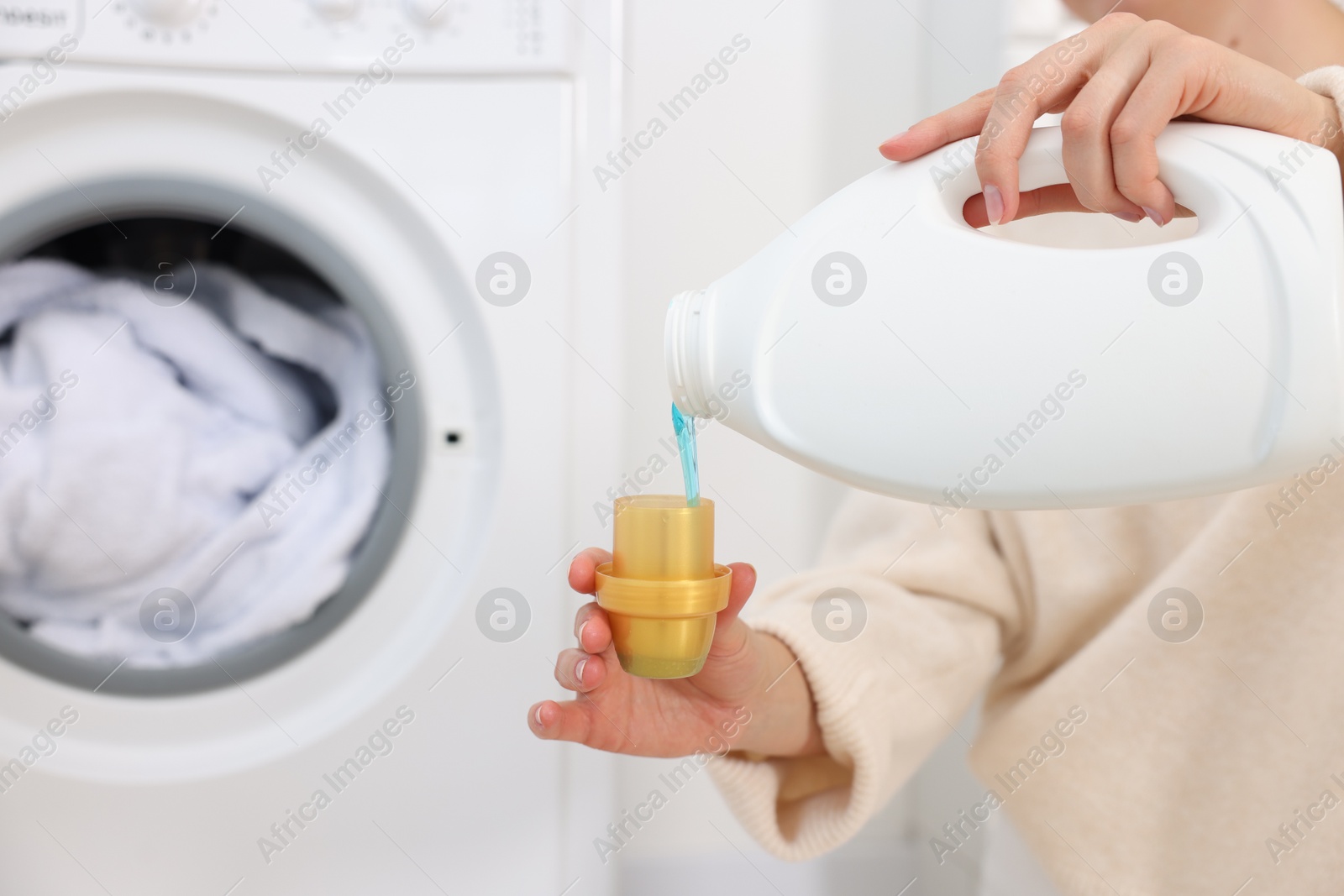 Photo of Woman pouring detergent into cap near washing machine in laundry room, closeup. Space for text