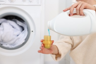 Photo of Woman pouring detergent into cap near washing machine in laundry room, closeup. Space for text