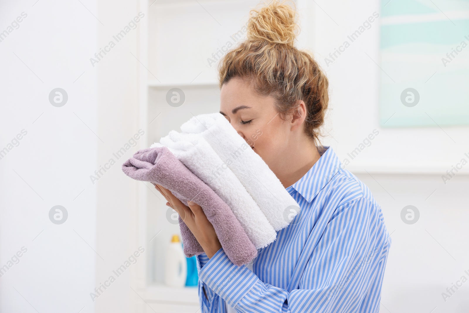 Woman with stack of clean laundry indoors Photo of Woman with stack of clean laundry indoors