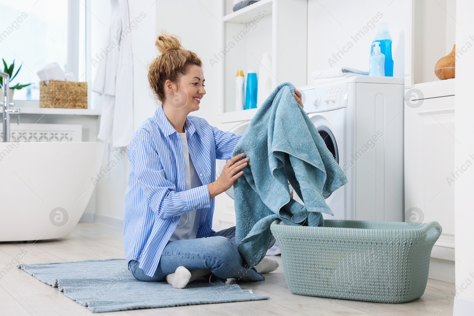 Woman with laundry near washing machine indoors Photo of Woman with laundry near washing machine indoors