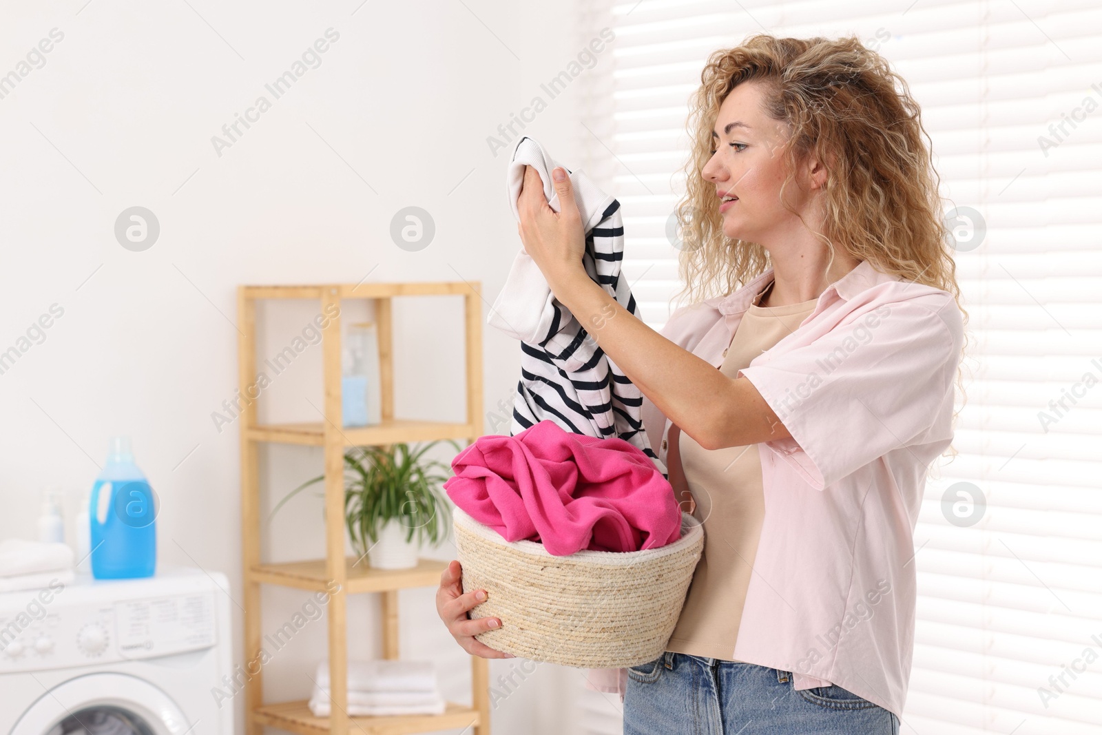 Photo of Woman with basket full of laundry indoors, space for text