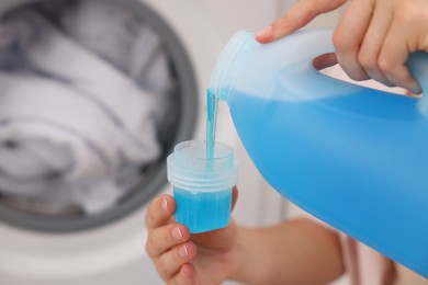Photo of Woman pouring detergent into cap near washing machine in laundry room, closeup. Space for text