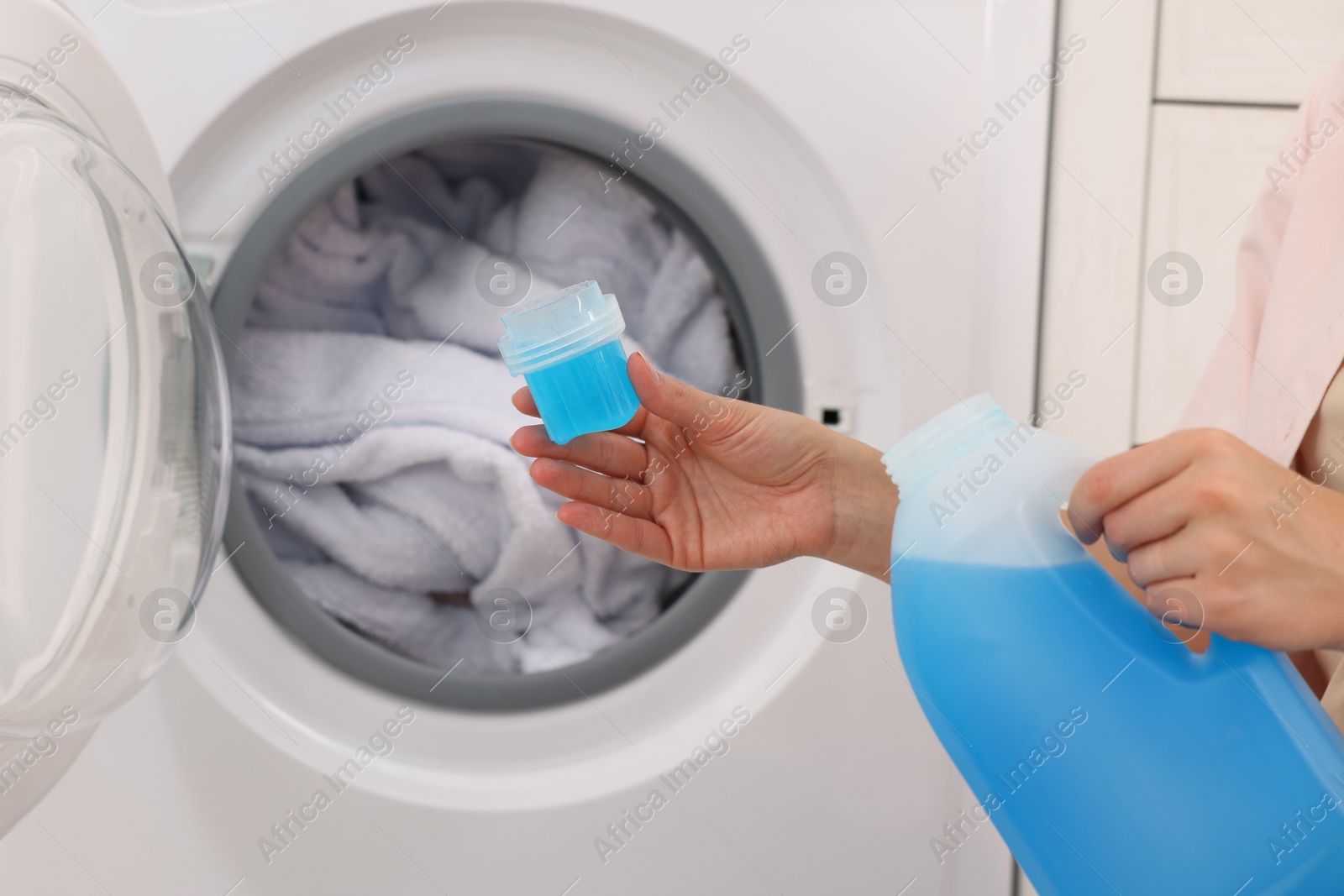Photo of Woman with detergent near washing machine indoors, closeup. Laundry day