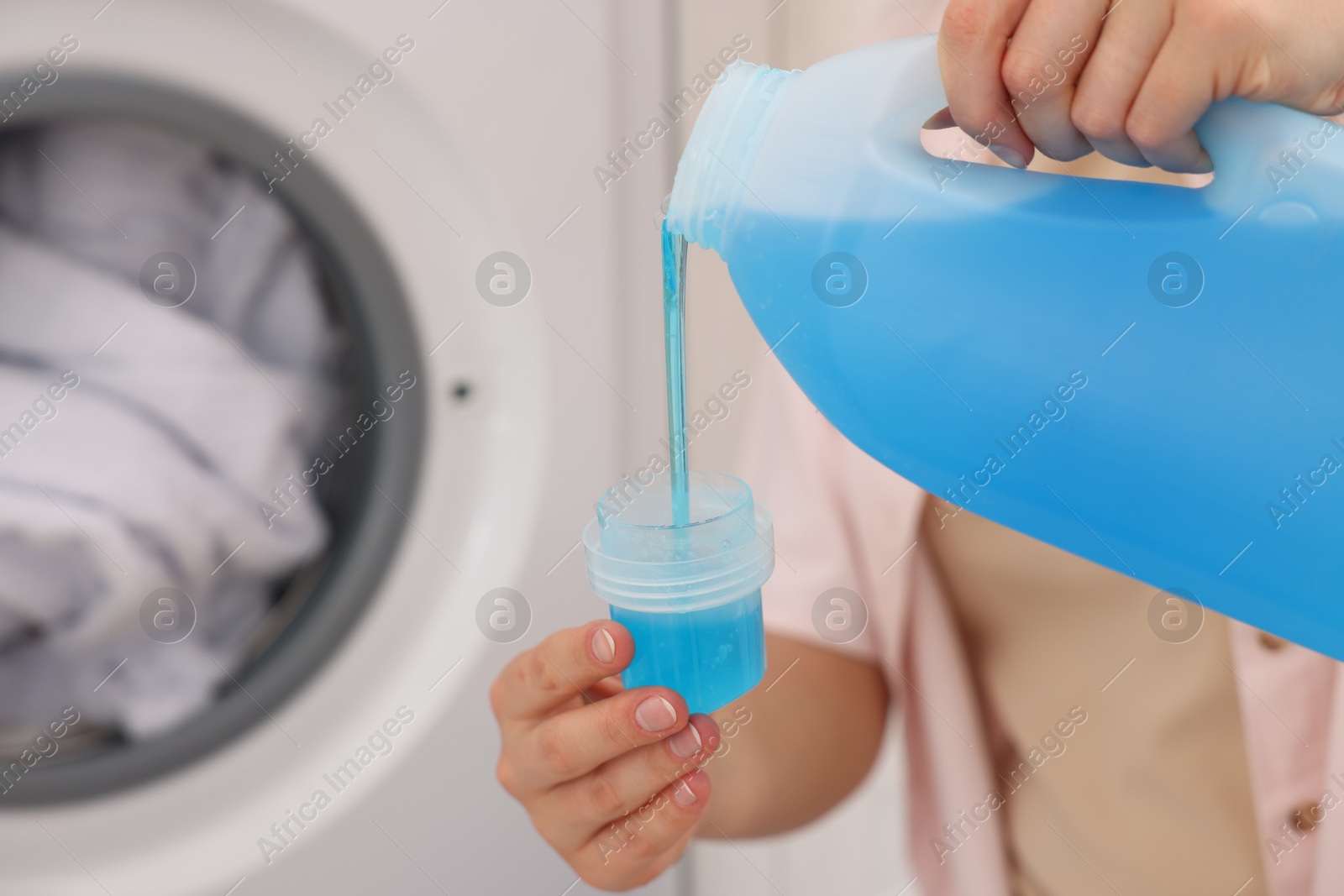 Photo of Woman pouring detergent into cap near washing machine in laundry room, closeup. Space for text