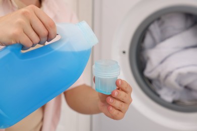 Photo of Woman pouring detergent into cap near washing machine in laundry room, closeup. Space for text