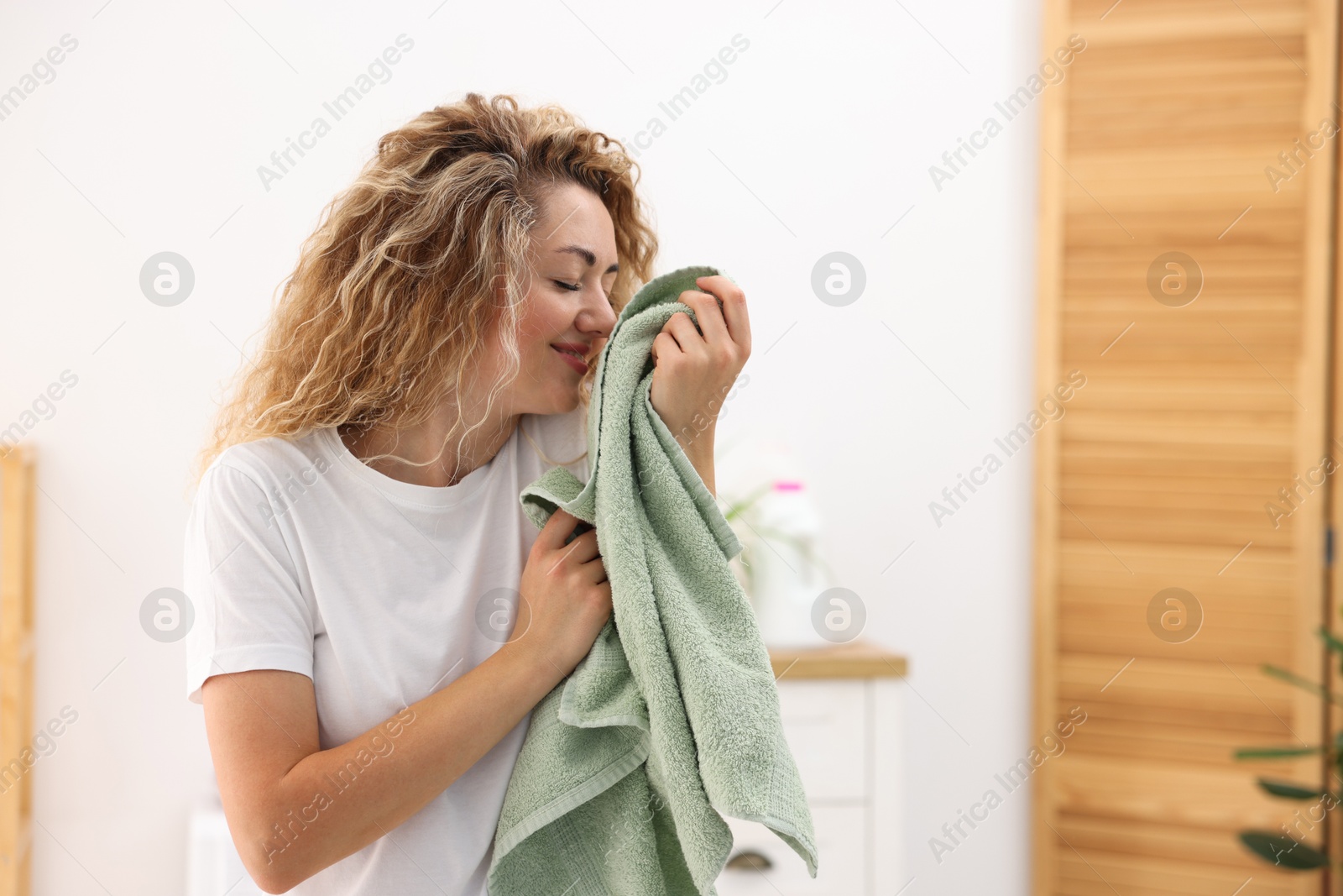 Photo of Happy woman with clean laundry indoors, space for text