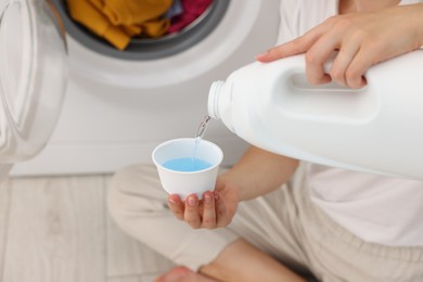 Photo of Woman pouring detergent into cap near washing machine in laundry room, closeup