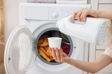 Photo of Woman pouring detergent into cap near washing machine in laundry room, closeup