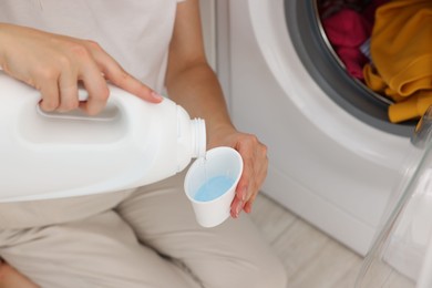 Photo of Woman pouring detergent into cap near washing machine in laundry room, closeup