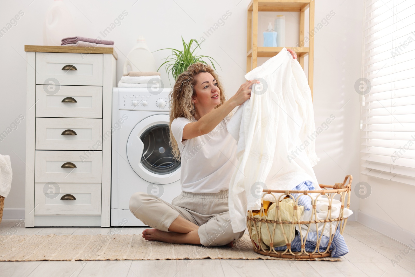 Woman with laundry near washing machine indoors Photo of Woman with laundry near washing machine indoors