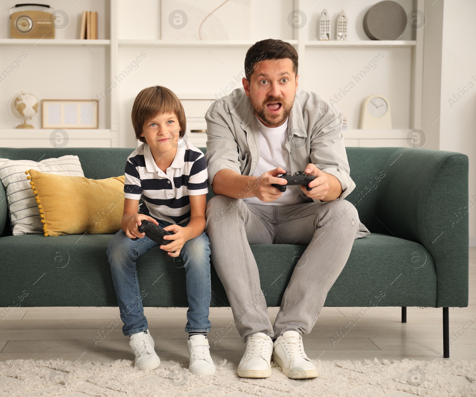 Father and son with controllers playing videogame on sofa at home Photo of Father and son with controllers playing videogame on sofa at home