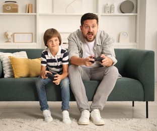 Photo of Father and son with controllers playing videogame on sofa at home