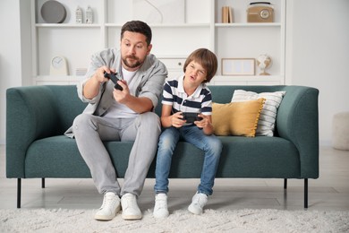 Photo of Father and son with controllers playing videogame on sofa at home