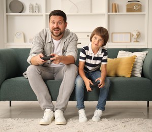 Photo of Father and son with controllers playing videogame on sofa at home
