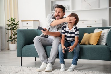 Photo of Father and son with controllers having fun while playing videogame on sofa at home