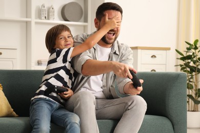 Photo of Father and son with controllers having fun while playing videogame on sofa at home