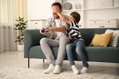 Photo of Father and son with controllers having fun while playing videogame on sofa at home