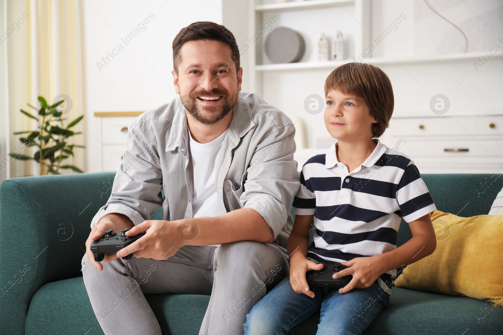 Father and son with controllers playing videogame on sofa at home Photo of Father and son with controllers playing videogame on sofa at home