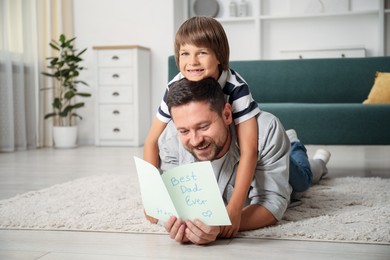 Photo of Happy Father's Day. Man reading card with phrase Best dad ever and his son hugging him at home. Space for text