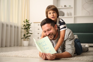Photo of Happy Father's Day. Man reading card with phrase Best dad ever and his son hugging him at home. Space for text