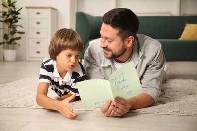 Photo of Happy Father's Day. Man reading card with phrase Best dad ever and his son hugging him at home