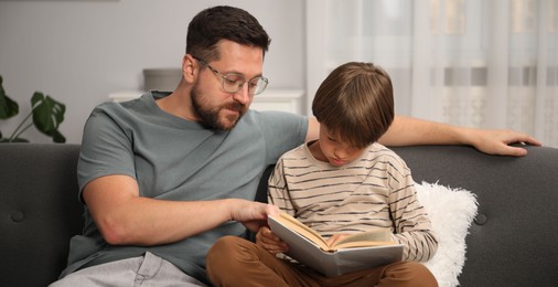 Photo of Father and son reading book together on sofa at home