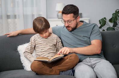 Photo of Father and son reading book together on sofa at home