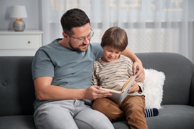 Photo of Father and son reading book together on sofa at home