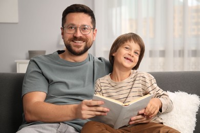 Photo of Father and son reading book together on sofa at home