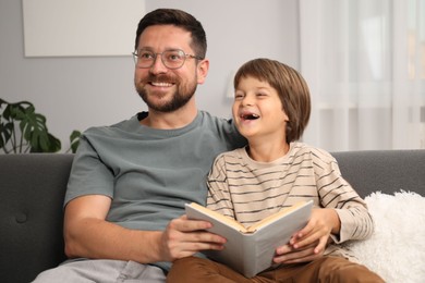 Photo of Father and son reading book together on sofa at home