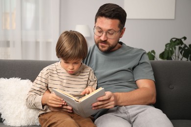 Photo of Father and son reading book together on sofa at home