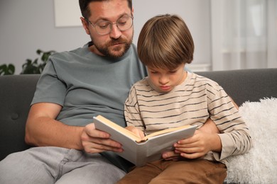 Photo of Father and son reading book together on sofa at home