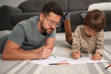Photo of Father and son drawing together on floor at home