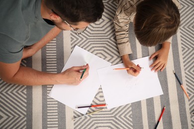 Photo of Father and son drawing together on floor at home, above view