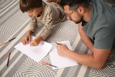 Photo of Father and son drawing together on floor at home