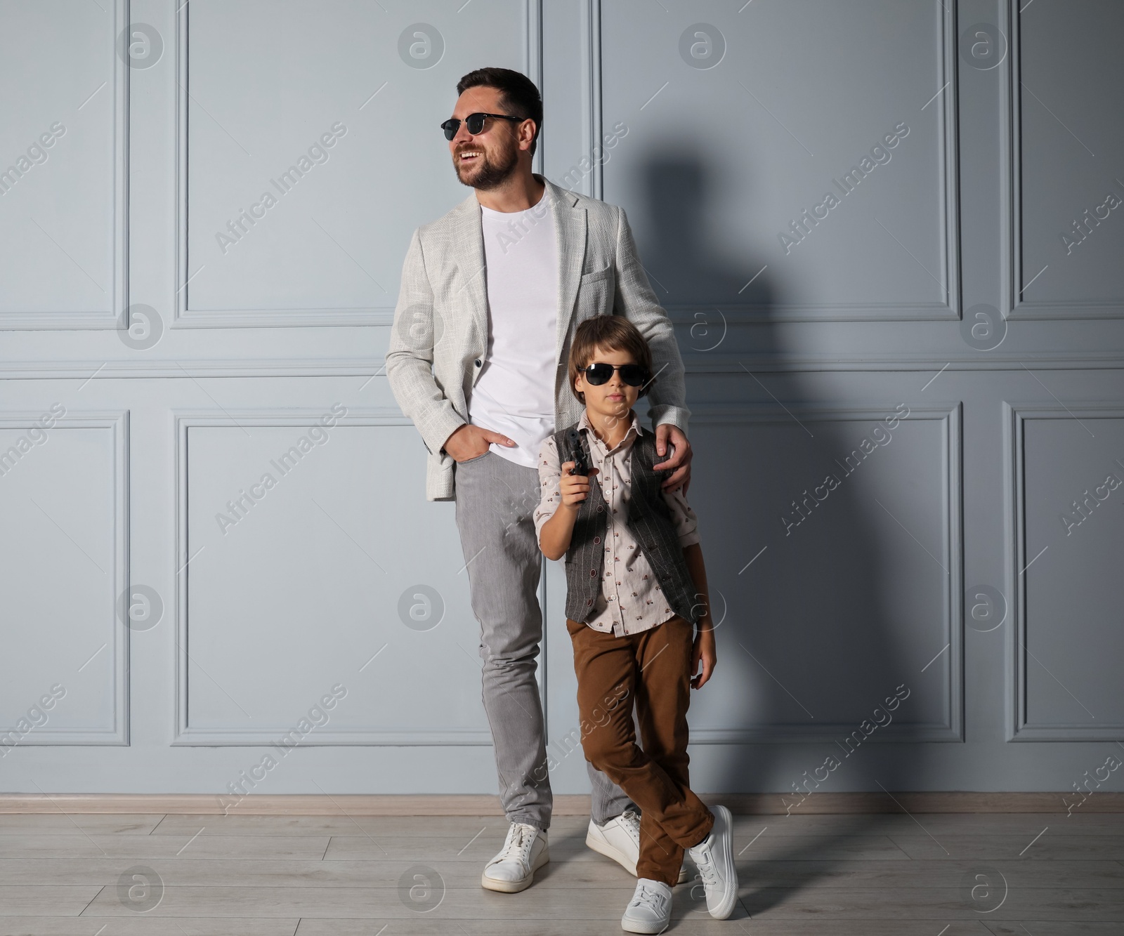 Father and son in stylish outfits posing near light wall Photo of Father and son in stylish outfits posing near light wall