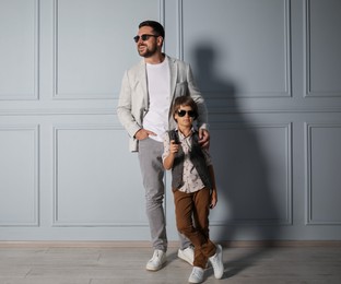 Photo of Father and son in stylish outfits posing near light wall