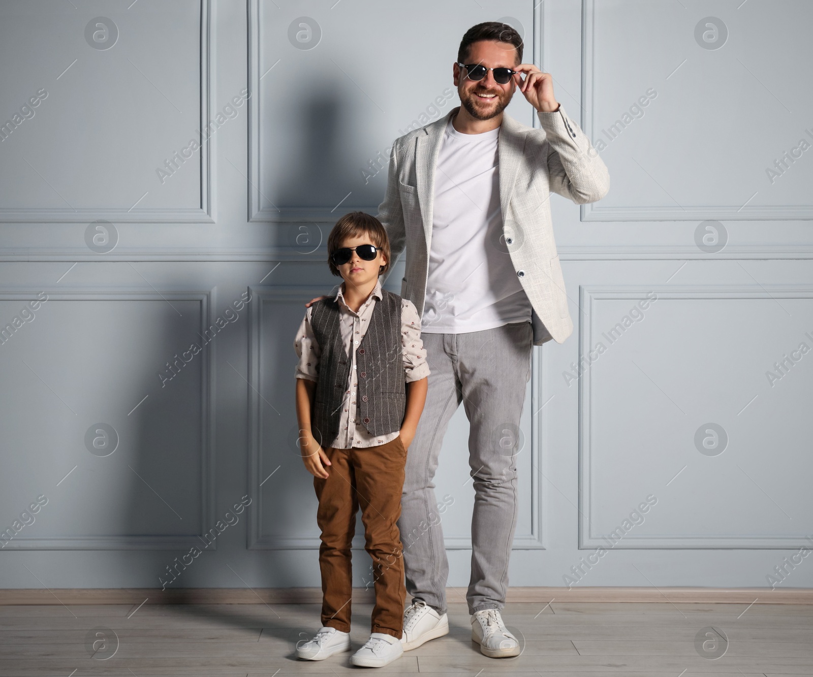 Father and son in stylish outfits posing near light wall Photo of Father and son in stylish outfits posing near light wall