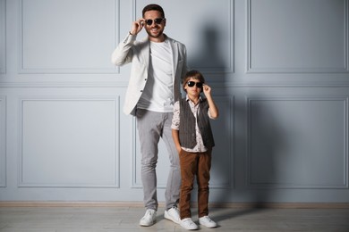 Photo of Father and son in stylish outfits posing near light wall
