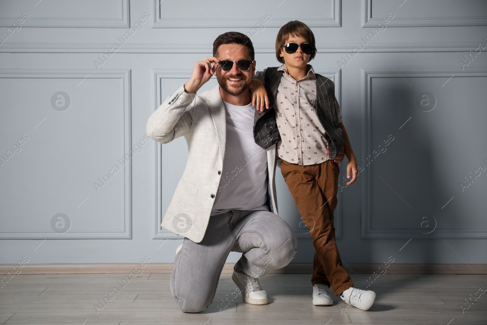 Photo of Father and son in stylish outfits posing near light wall